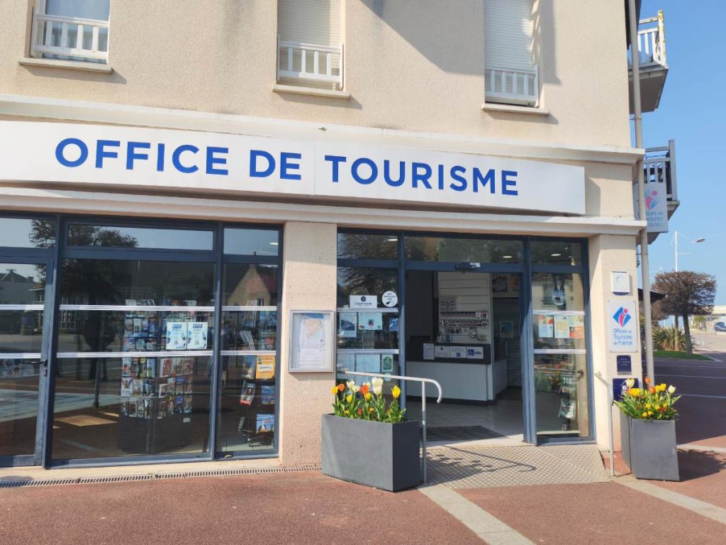 Façade de l'Office de Tourisme de Courseulles-sur-mer avec bacs de fleurs et brochures visibles.