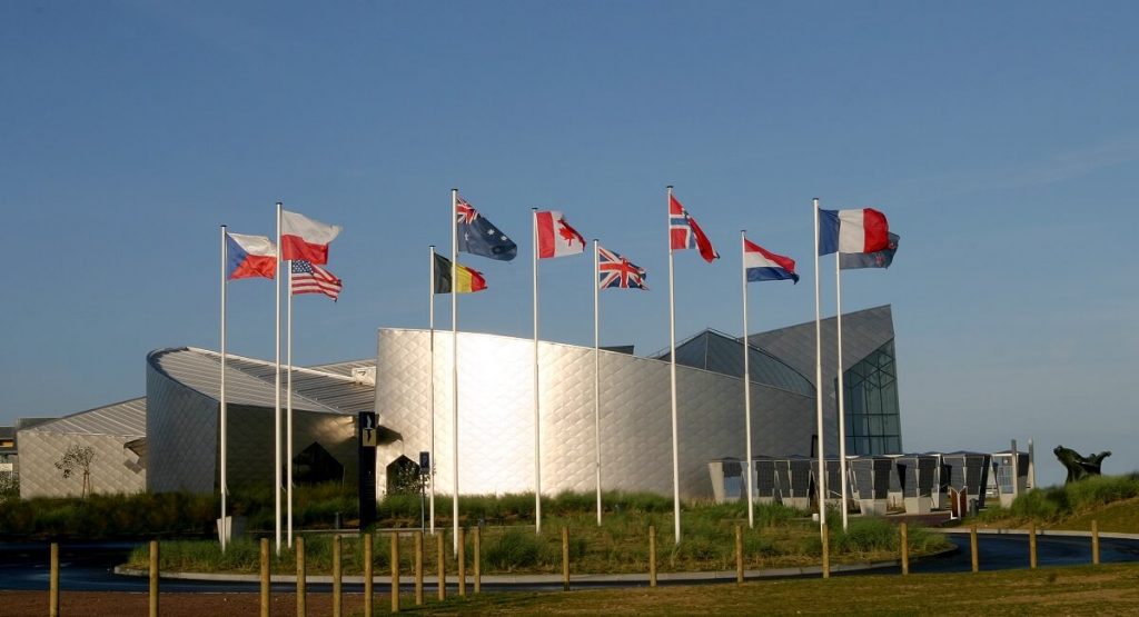 Le bâtiment du centre : une architecture moderne aux parodies arrondies couleur aluminium, disposée de manière à former le dessin d'une feuille d'érable, au premier plan flottent les drapeaux des pays alliées. - crédit : cjb, G. Wait