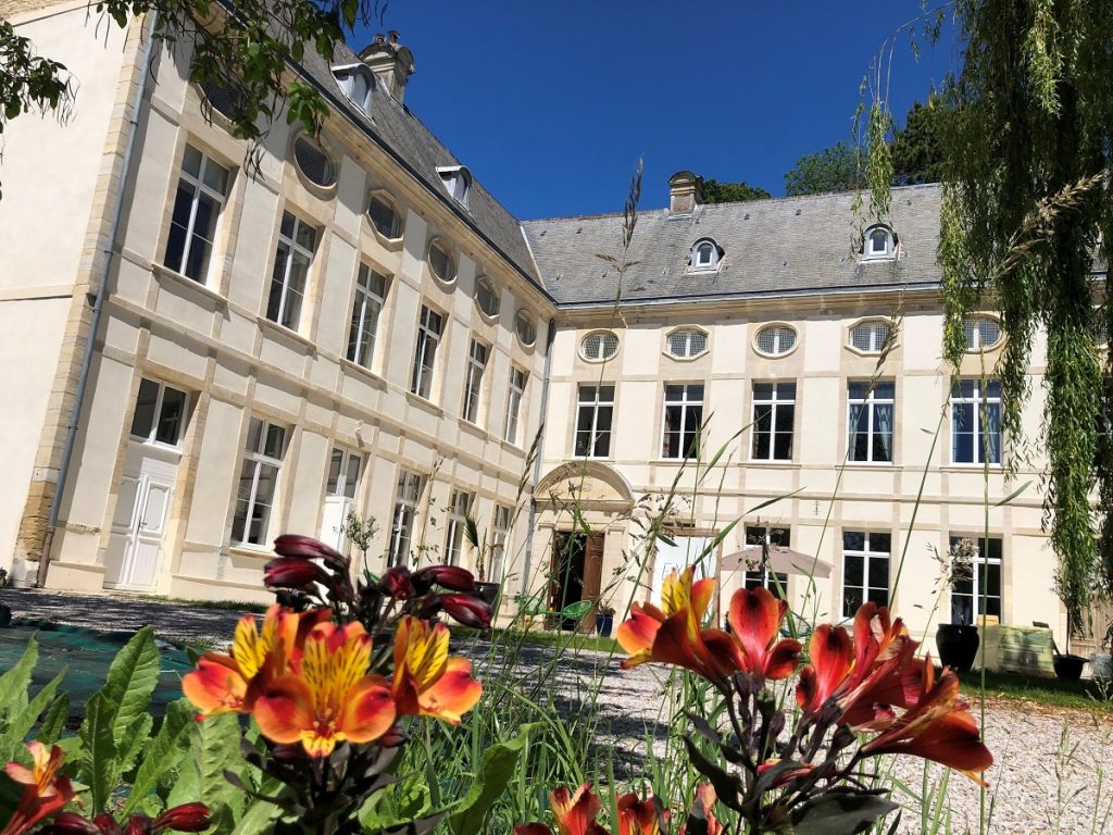 Main facade and facade of the north wing of Château de Reviers on a bright blue day.