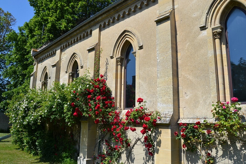 The exterior facade of the former Protestant church in Cresserons: it is punctuated by alternating round-arched windows and buttresses. The façade is rendered and red roses in bloom grow all along the façade.