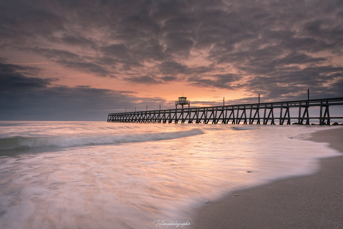 In a twilight with purplish reflections, the jetty at Luc-sur-Mer juts out into the waves, the foam of which comes to rest on the sand.