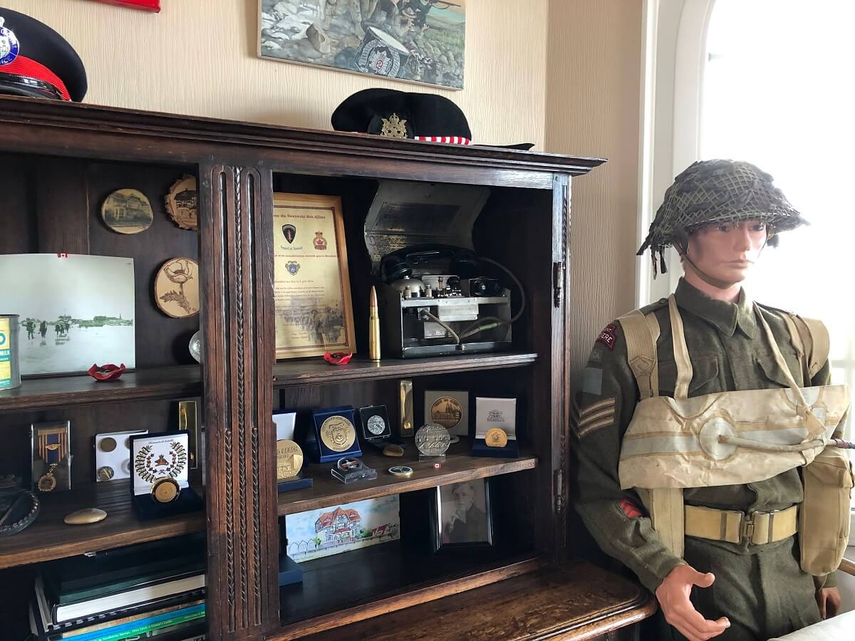 A l'intérieur de la maison des Canadiens, un buffet en bois foncé où sont exposé des décorations militaires. A droite du meuble le mannequin d'un soldat de la seconde Guerre Mondiale en uniforme.