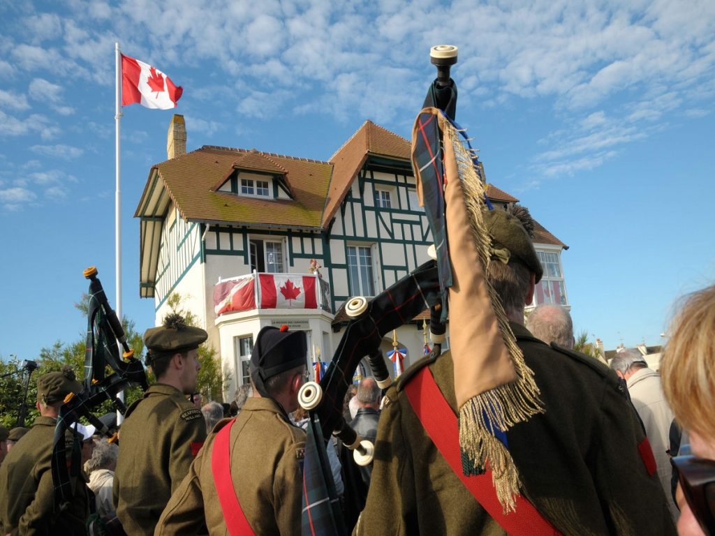 Cérémonie du D-Day devant la maison des Canadien de Bernières, au premier plan, de dos, deux joueurs de cornemuse en uniforme. - crédit : Francois Dupont