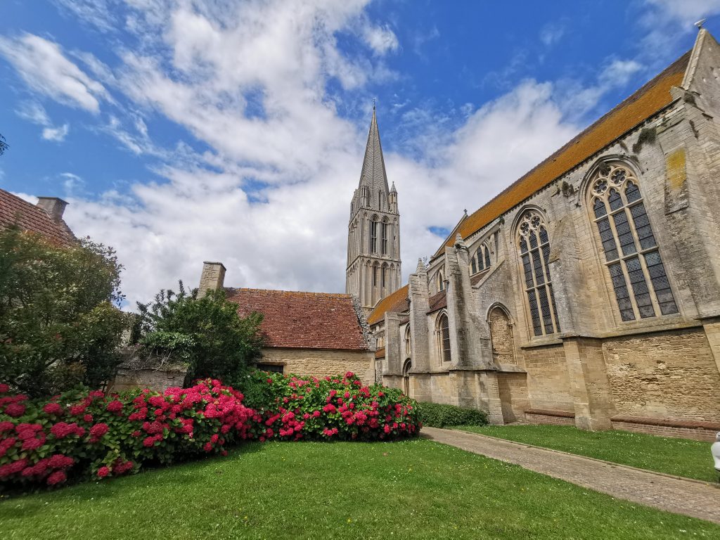 Vue de l'église de Bernières-sur-Mer, le toit est fait de tuile, la façade de la nef possède de grandes bais en arc brisé, elle est renforcée par trois arcs boutants. - crédit : Nathalie Papouin