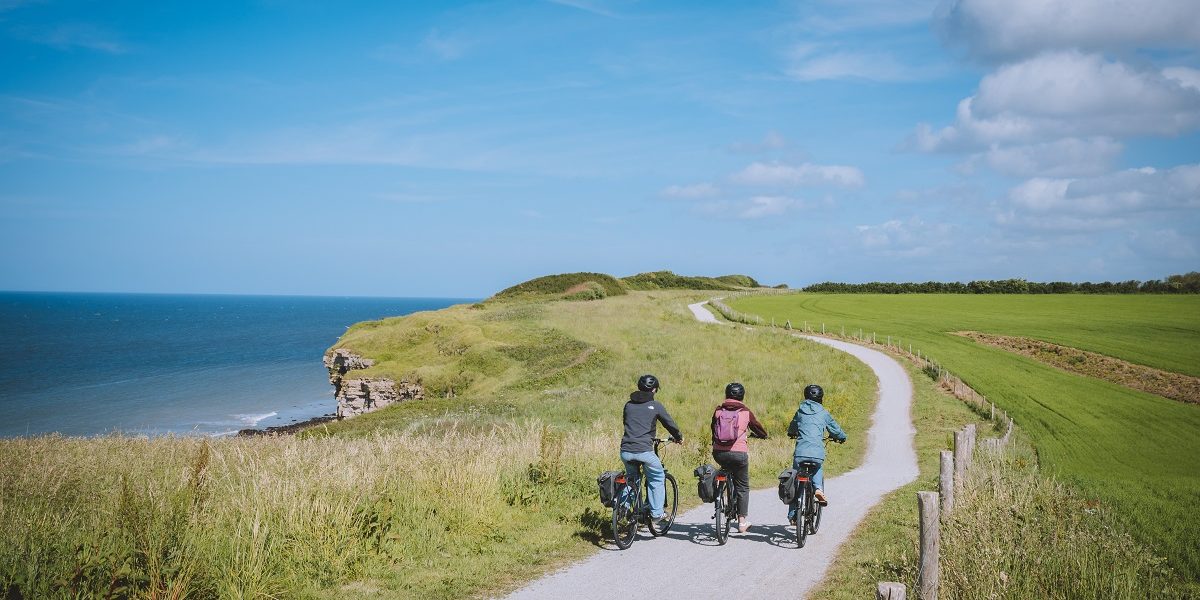 Trois cyclistes sur la voie verte de la Liberté (Vélomaritime) longeant les falaises et la mer.