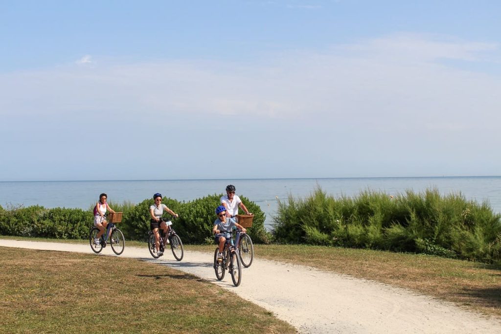 Groupe de quatre cyclistes sur une piste cyclable bordée de tamaris avec la mer en arrière-plan.