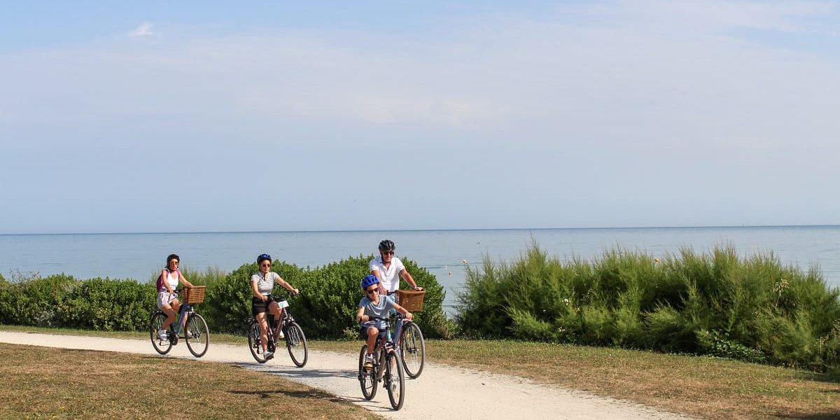 Groupe de quatre cyclistes sur une piste cyclable bordée de tamaris avec la mer en arrière-plan.